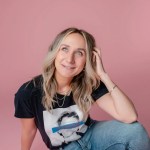 Headshot image of a blond woman against a pink background, wearing a black t-shirt and jeans
