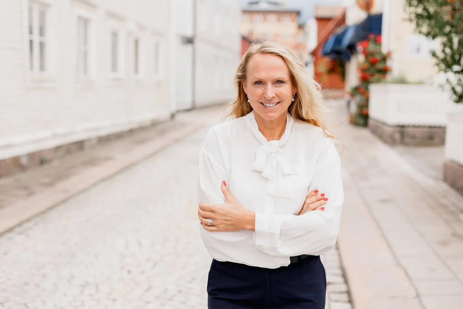 Security consultant in a white ruffle blouse and navy pants standing on a cobblestone street, smiling